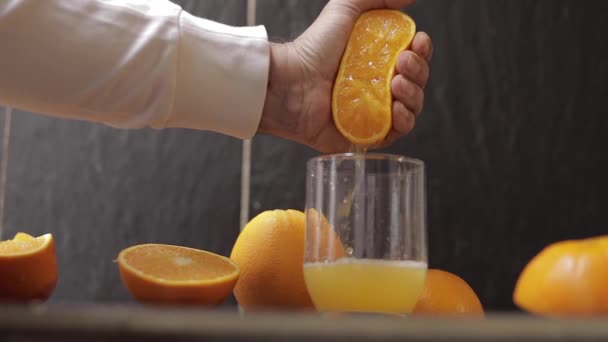 Ręka człowieka wciska sok z pomarańczy w szkło. Mężczyzna trzyma połowę pomarańczy pod ręką. — Wideo stockowe