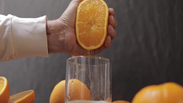 La mano del hombre exprimen el jugo de la naranja en el vaso. El hombre tiene la mitad de naranja en la mano — Vídeo de stock