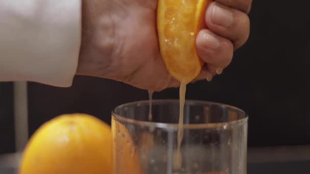 La mano del hombre exprimen el jugo de la naranja en el vaso. El hombre tiene la mitad de naranja en la mano — Vídeos de Stock