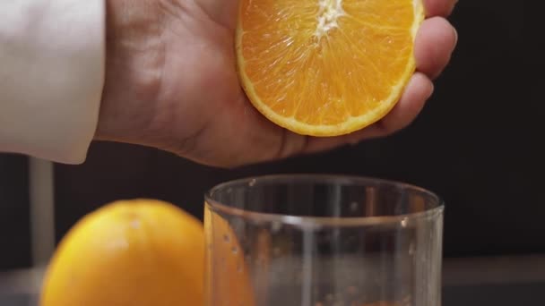 Hand of man squeeze juice from an orange into glass. Man hold half of orange on hand — Stock Video