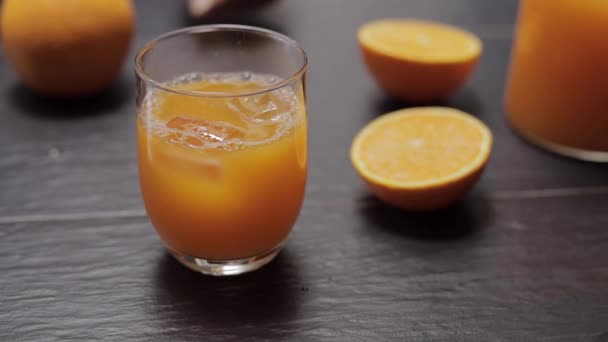 Verre avec jus d'orange frais et glace sur la table dans la cuisine — Video