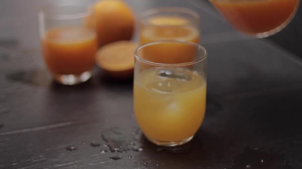 Vidro com suco de laranja fresco e gelo na mesa na cozinha — Vídeo de Stock