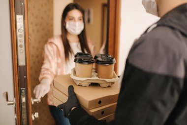 Maskeli ve eldivenli müşterilere pizza ve kahve getiren adam. Kadın kapıyı aç ve siparişi al. Coronavirus teması