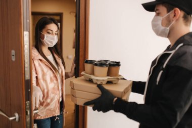Maskeli ve eldivenli müşterilere pizza ve kahve getiren adam. Kadın kapıyı aç ve siparişi al. Coronavirus teması