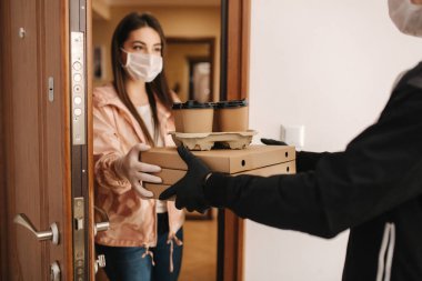 Maskeli ve eldivenli müşterilere pizza ve kahve getiren adam. Kadın kapıyı aç ve siparişi al. Coronavirus teması