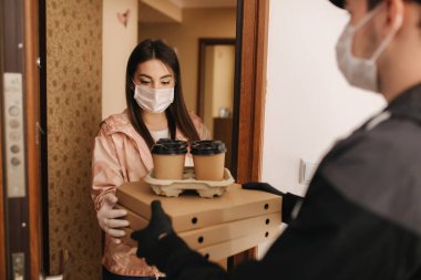 Maskeli ve eldivenli müşterilere pizza ve kahve getiren adam. Kadın kapıyı aç ve siparişi al. Coronavirus teması