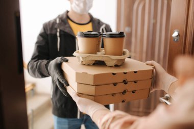 Maskeli teslimatçı ve eldivenli adam müşteriye pizza ve kahve veriyor. Evde kal.