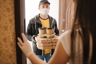 Maskeli teslimatçı ve eldivenli adam müşteriye pizza ve kahve veriyor. Evde kal.