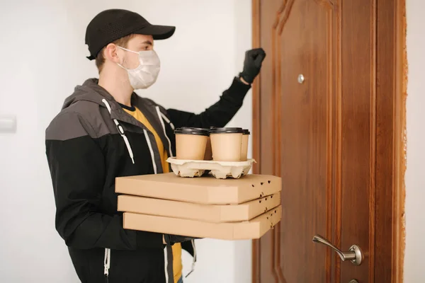 Man leverans pizza och kaffe till kund i mask och handskar. Coronavirus tema. Man knackar på dörrar — Stockfoto
