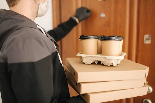 Man leverans pizza och kaffe till kund i mask och handskar. Coronavirus tema. Man knackar på dörrar — Stockfoto