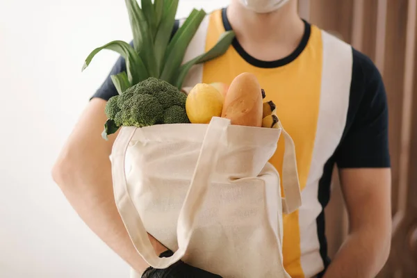 Доставка человек в маске и перчатках принести свежие продукты питания для клиентов домой. Сиди дома. Концепция покупок — стоковое фото