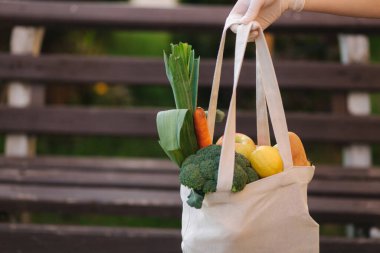 Tıbbi eldivenlerdeki kadın eli taze yiyecek, sebze, meyve ve ekmek dolu çantayı tutuyor. Marketten sonra.
