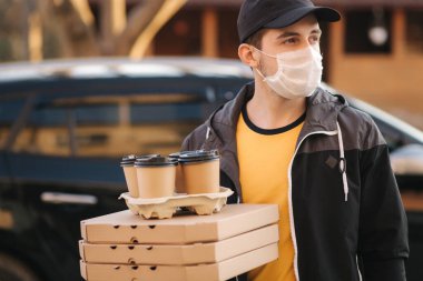 Koruyucu maskeli kurye ve tıbbi eldivenler müşteriyi bekliyor. Teslimatçı çocuk pizza ve kahveyi arabanın önünde bekletiyor. Teslimat servisi karantina altında. Coronavirus covid-19 teması