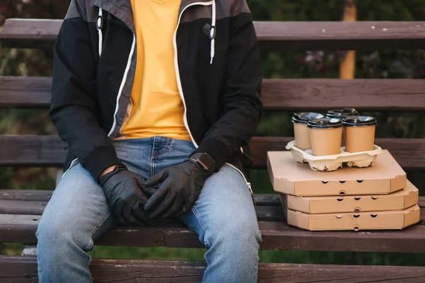 Courier en masque protecteur et gants médicaux livre pizza et café. Livraison garçon assis sur le banc et attendre le client. Service de livraison en quarantaine. Coronavirus covid-19 thème — Photo