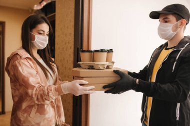 Maskeli ve eldivenli müşterilere pizza ve kahve getiren adam. Kadın kapıyı aç ve siparişi al. Coronavirus teması