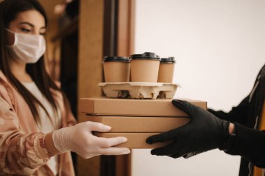 Maskeli ve eldivenli müşterilere pizza ve kahve getiren adam. Kadın kapıyı aç ve siparişi al. Coronavirus teması