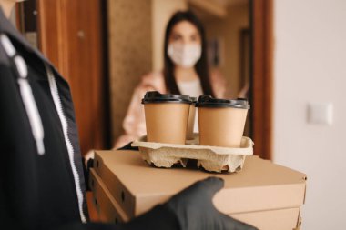 Maskeli ve eldivenli müşterilere pizza ve kahve getiren adam. Kadın kapıyı aç ve siparişi al. Coronavirus teması