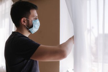 Koruyucu maskeli genç adam temiz hava almak için pencereyi açtı. Coronavirus teması