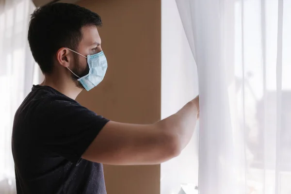 Ung man i skyddande mask hemma öppna fönster för att andas frisk luft. Tema för Coronavirus — Stockfoto