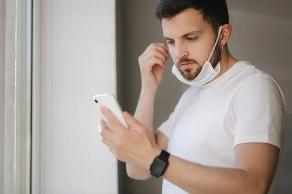 Young man take off protective mask and use smartphone. End of quarantine. Coronavirus theme