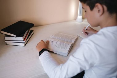 Masada oturan genç çocuk kitabı okudu ve deftere yazdı. Karantina sırasında evde çalış