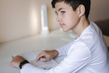 Genç çocuk masada oturuyor ve kitabı okuyor. Karantina sırasında evde çalış