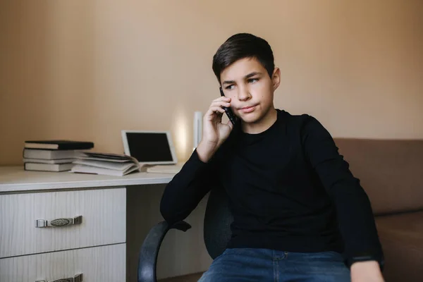 Porträt eines jungen Teenagers, der zu Hause telefoniert. Hintergrund von Tablet und Büchern — Stockfoto