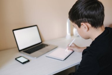 Evde tablete resim çizen yakışıklı bir çocuk. Genç çocuk iş için tablet kullanıyor. Öğrenci evde tablet, dizüstü bilgisayar, akıllı telefon kullanarak ders çalışıyor.