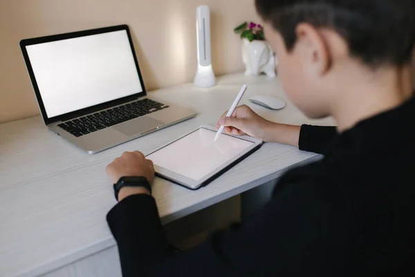 Красивый мальчик рисует дома на планшете. Подросток использует планшет для работы. Школьник учится дома с помощью планшета, ноутбука, смартфона — стоковое фото