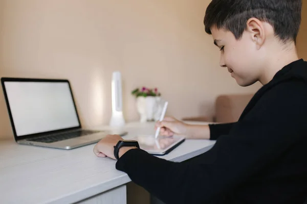 Knappe jongen die thuis op een tablet tekent. Tienerjongen gebruiken tablet voor het werk. Schooljongen thuis studeren met behulp van tablet, laptop, smartphone — Stockfoto