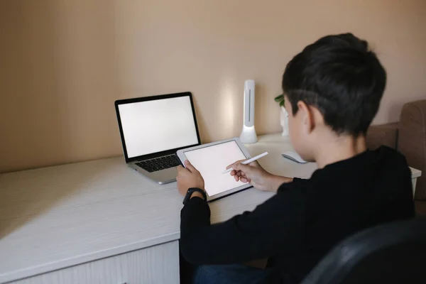 Knappe jongen die thuis op een tablet tekent. Tienerjongen gebruiken tablet voor het werk. Schooljongen thuis studeren met behulp van tablet, laptop, smartphone — Stockfoto