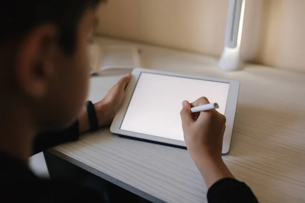 Красивый мальчик рисует дома на планшете. Подросток использует планшет для работы. Школьник учится дома с помощью планшета, ноутбука, смартфона — стоковое фото