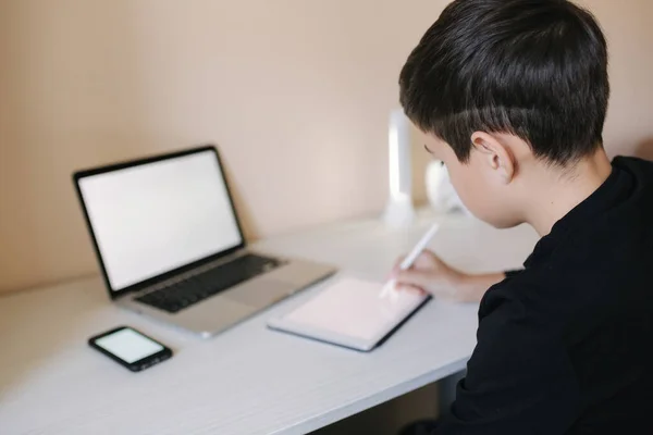 Knappe jongen die thuis op een tablet tekent. Tienerjongen gebruiken tablet voor het werk. Schooljongen thuis studeren met behulp van tablet, laptop, smartphone — Stockfoto