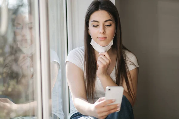 Mujer joven quitarse la máscara protectora y el uso de teléfono inteligente. Fin de la cuarentena. Tema Coronavirus — Foto de Stock