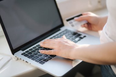Bilgisayarlı telefon ve kredi kartıyla genç bir kadının online alışverişini kapat. Pencere kenarındaki dizüstü bilgisayar