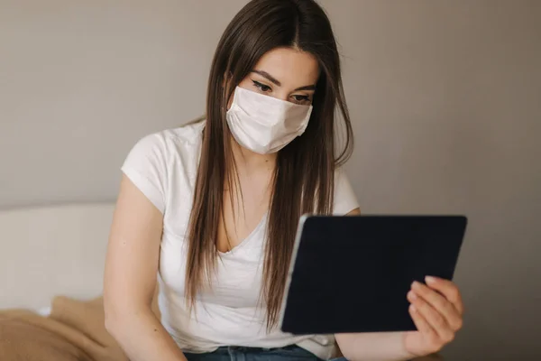 Jovem mulher em máscara usar comprimido na cama. Feminino assistir vídeo online durante a quarentena. Estudante Estudo em casa — Fotografia de Stock