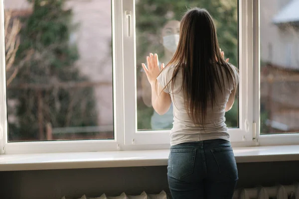 Visszapillantás a fiatal nőre orvosi maszkban maradjon az ablaknál a karanténban. A nő kinézett az ablakon. Kovid-19 — Stock Fotó