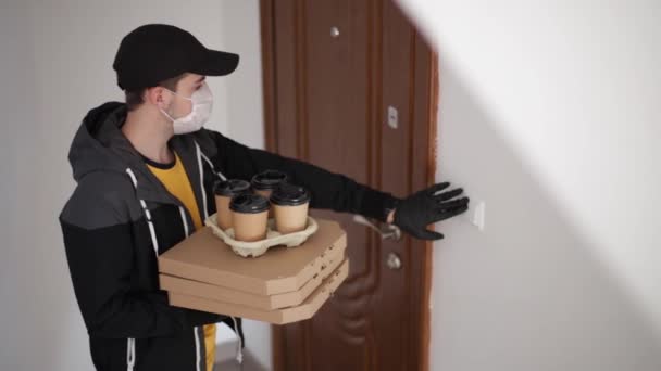Человек доставляет пиццу и кофе клиенту в маске и перчатках. Тема коронавируса. Мужчина звонит в дверь, женщина открывает дверь — стоковое видео
