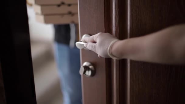 El repartidor con máscara y guantes da pizza y café al cliente femenino. Una mujer abre la puerta para tomar el orden. Vista desde el apartamento. Quédate en casa. — Vídeos de Stock