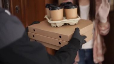 Maskeli ve eldivenli müşterilere pizza ve kahve getiren adam. Kadın kapıyı aç ve siparişi al. Coronavirus teması