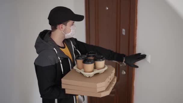 Man levering pizza en koffie aan de klant in masker en handschoenen. Coronavirus thema. Man belt de deurbel vrouw open deur — Stockvideo