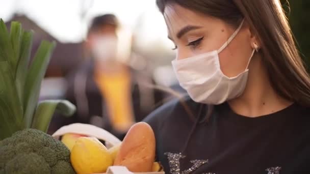 Kurir bertopeng pelindung dan sarung tangan medis memberikan makanan segar untuk pelanggan wanita. Layanan pengiriman di bawah karantina. Tema Coronavirus covid-19 — Stok Video