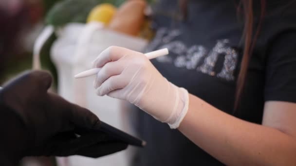 Slimme voedselvoorziening. Man met medisch masker en handschoenen die vers voedsel overhandigen aan jonge vrouwelijke klanten die een koeriersdienst thuis krijgen. Koerier met tablet, meld u aan. Vrouwelijke orde voedsel — Stockvideo