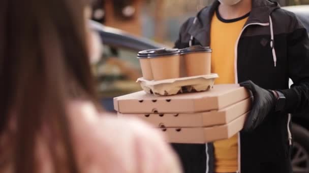 Mujer joven en máscara protectora y máscara médica tomar la orden del repartidor fuera. Entrega de comida en cuarentena. Mensajero traer pizza y café para el cliente — Vídeos de Stock