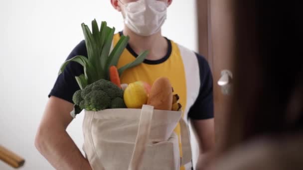 El repartidor con máscara y guantes trae comida fresca a los clientes a casa. Quédate en casa. Concepto de compras online — Vídeo de stock