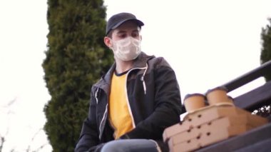 Koruyucu maskeli kurye ve tıbbi eldivenler pizza ve kahve getiriyor. Teslimatçı çocuk müşteriye yedek kulübesinde oturuyor. Teslimat servisi karantina altında. Coronavirus covid-19 teması