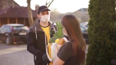Koruyucu maskeli ve tıbbi eldivenli kurye bayan müşterilere taze yiyecek getiriyor. Teslimat servisi karantina altında. Coronavirus covid-19 teması