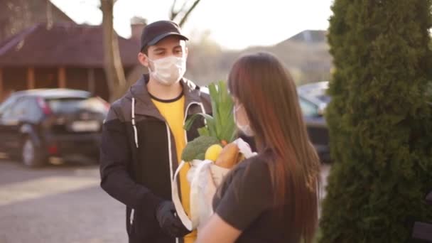 Koruyucu maskeli ve tıbbi eldivenli kurye bayan müşterilere taze yiyecek getiriyor. Teslimat servisi karantina altında. Coronavirus covid-19 teması — Stok video