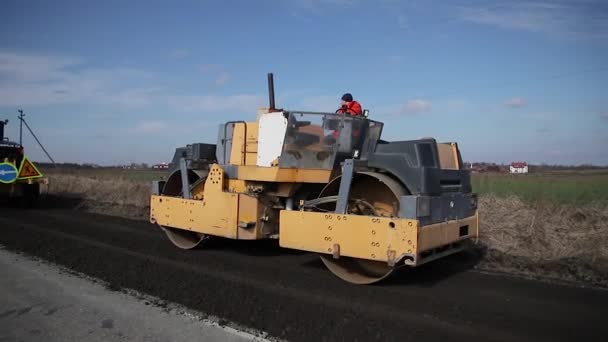 El pavimentador se mueve en una carretera plana de nueva construcción, embistiendo y nivelando. Aserradero de asfalto aplicando asfalto en la carretera de la ciudad reparada — Vídeos de Stock