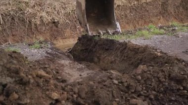 Kazı kazıcı kir yığınının üzerine atlıyor ve temizliyor. Vinçteki maşa inşaat malzemeleri taşıyor. Gevşek maddeler. Ormanın arka planı